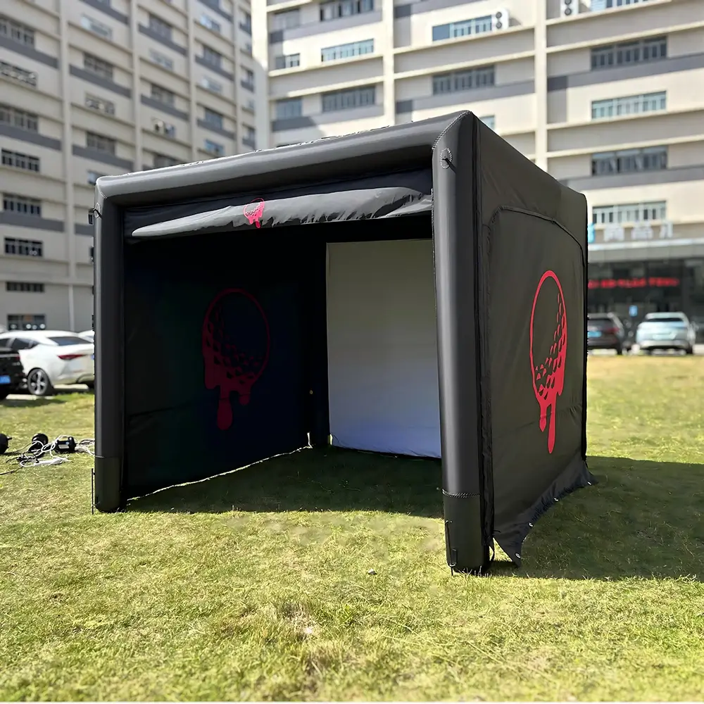 Black air-sealed inflatable golf simulator enclosure set up on outdoor grass with red golf ball graphic.